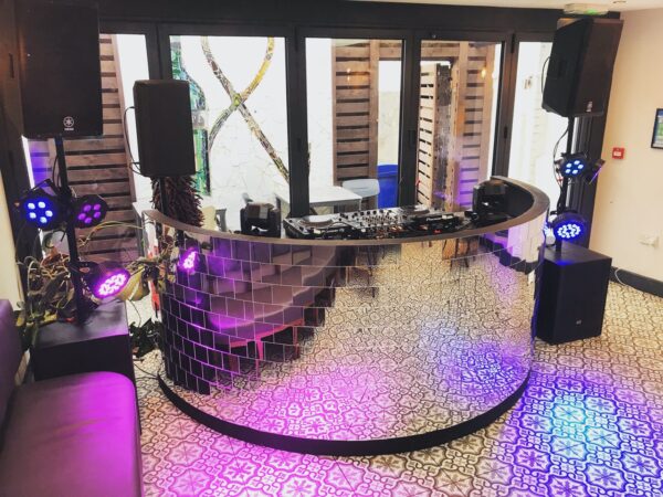 Premium mirrorball DJ booth setup with six LED par cans, small moving head lights, dual subwoofers, and pro audio tops for a wedding dancefloor.