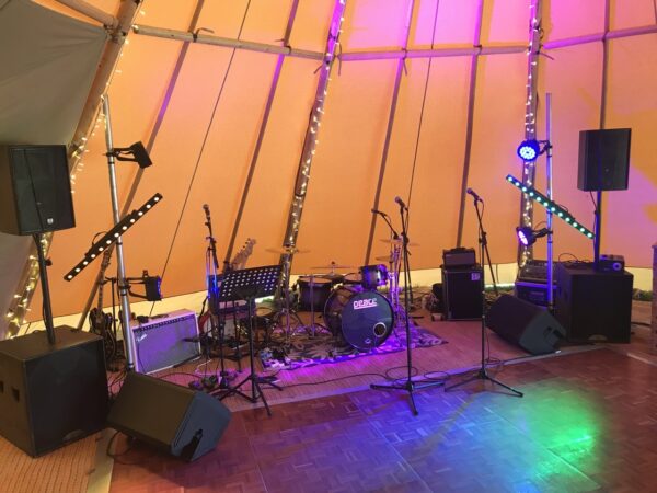 Complete live wedding band production sound stage featuring multi-channel digital mixing desk, active floor monitors, microphone stands, and industrial lighting totems.