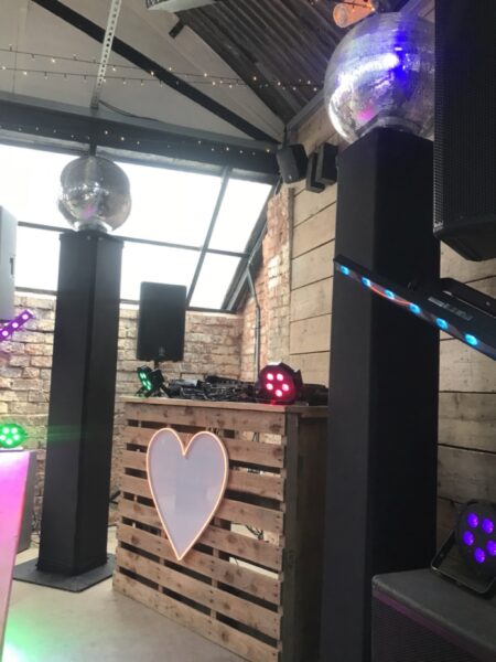 Sleek, minimalist dual PA speakers on neat stands with a compact laptop and tablet audio connectivity kit set up for a DIY wedding playlist.